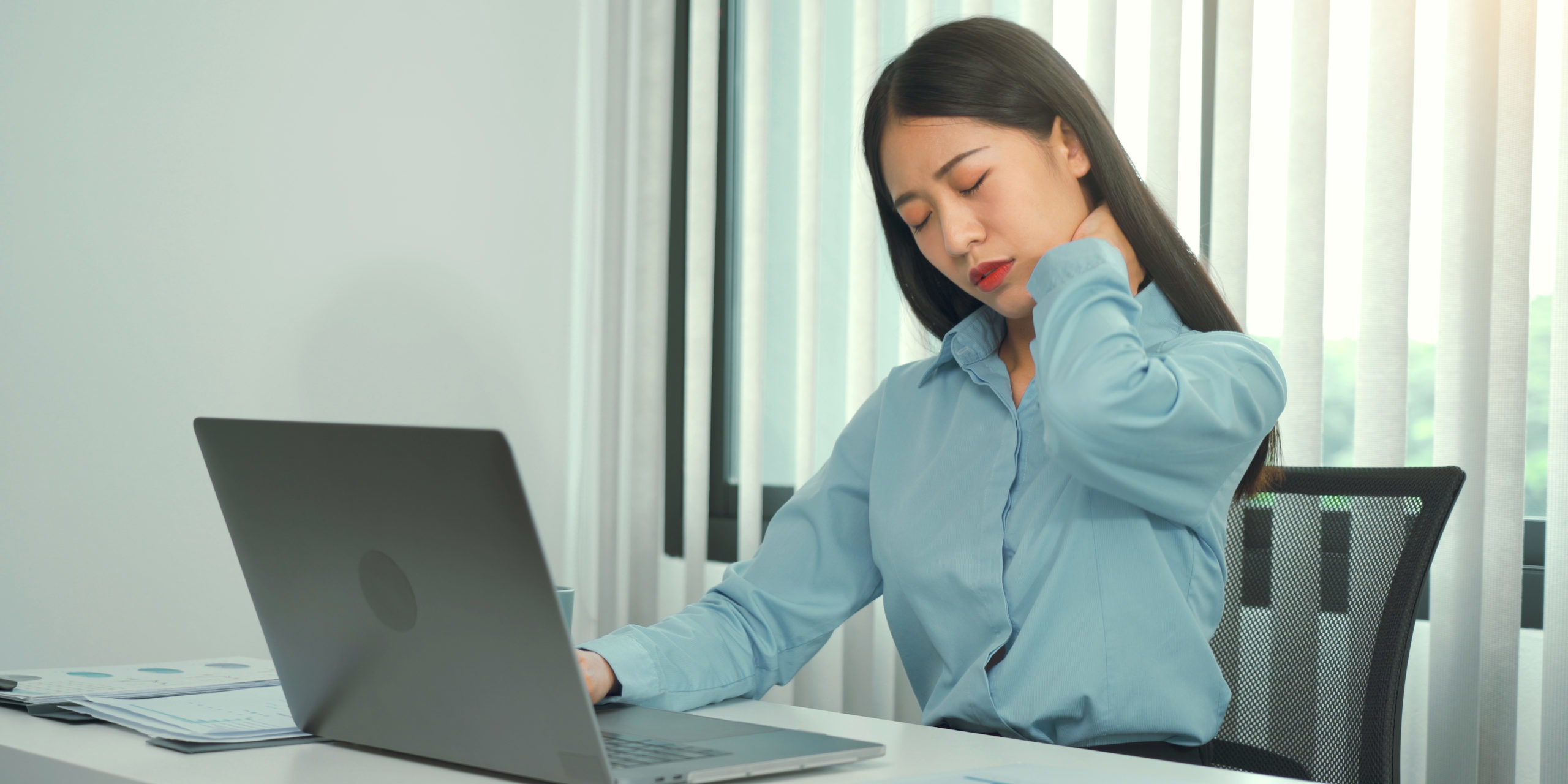Young asian woman is sitting at work and has pain in her neck wh Sitting at desk