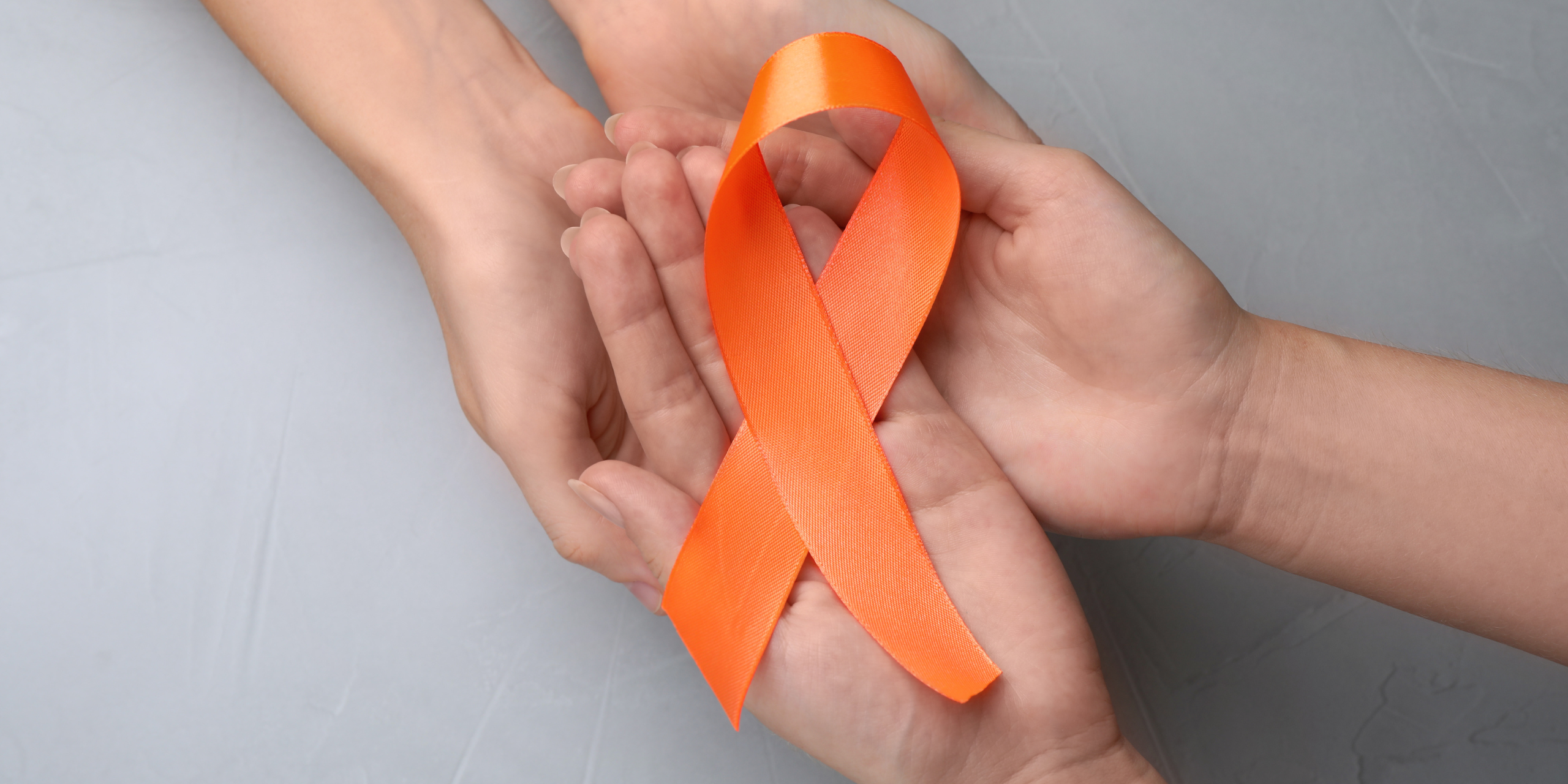 Two people reaching for each other's hands with a MS orange ribbon nestled on top of the palms. This represents Synergy Physical Therapy and Wellness' efforts in providing physical therapy that benefits the stages of MS